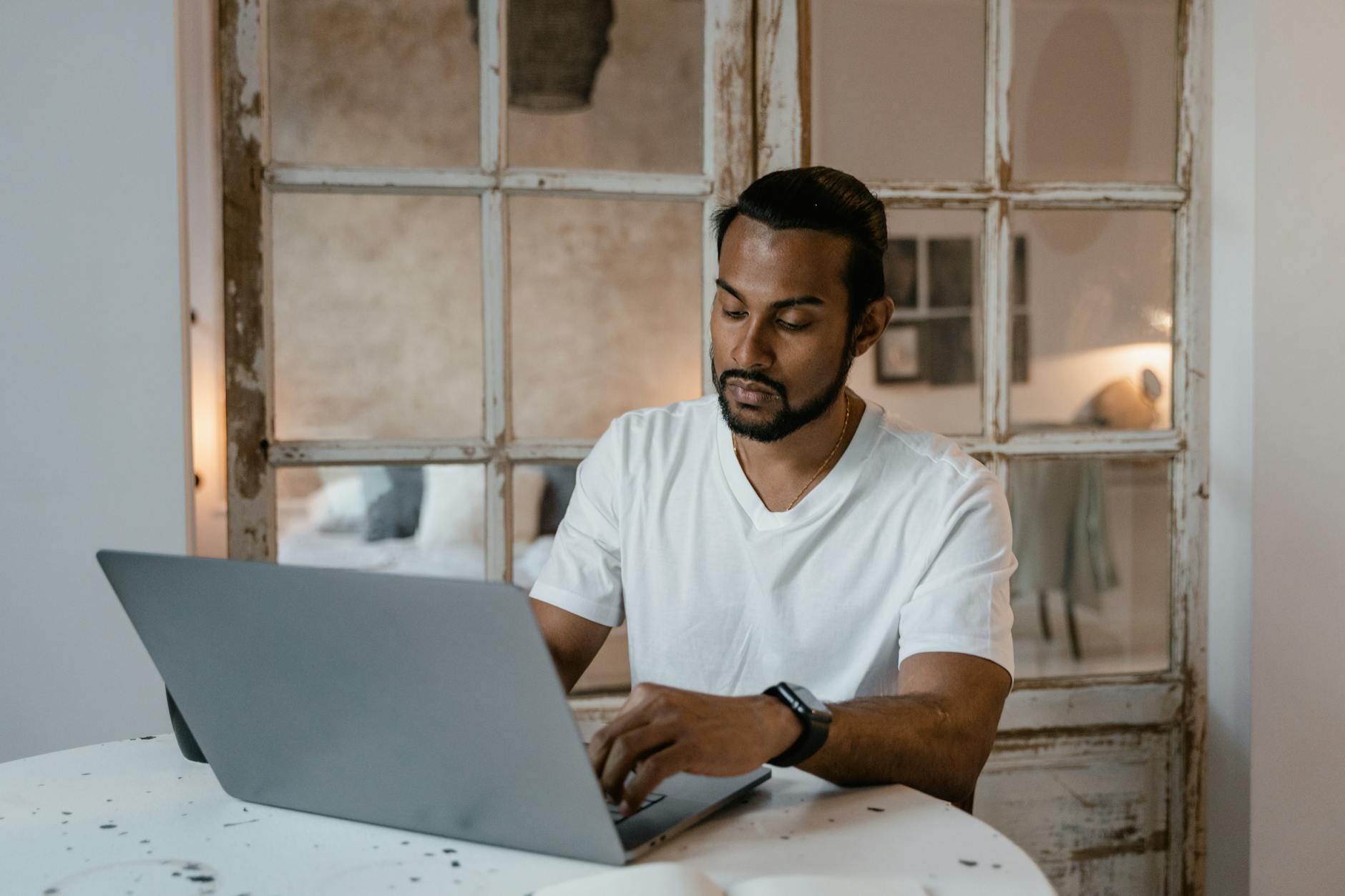 Brodaty mężczyzna pracuje na laptopie przy biurku w domowym zaciszu