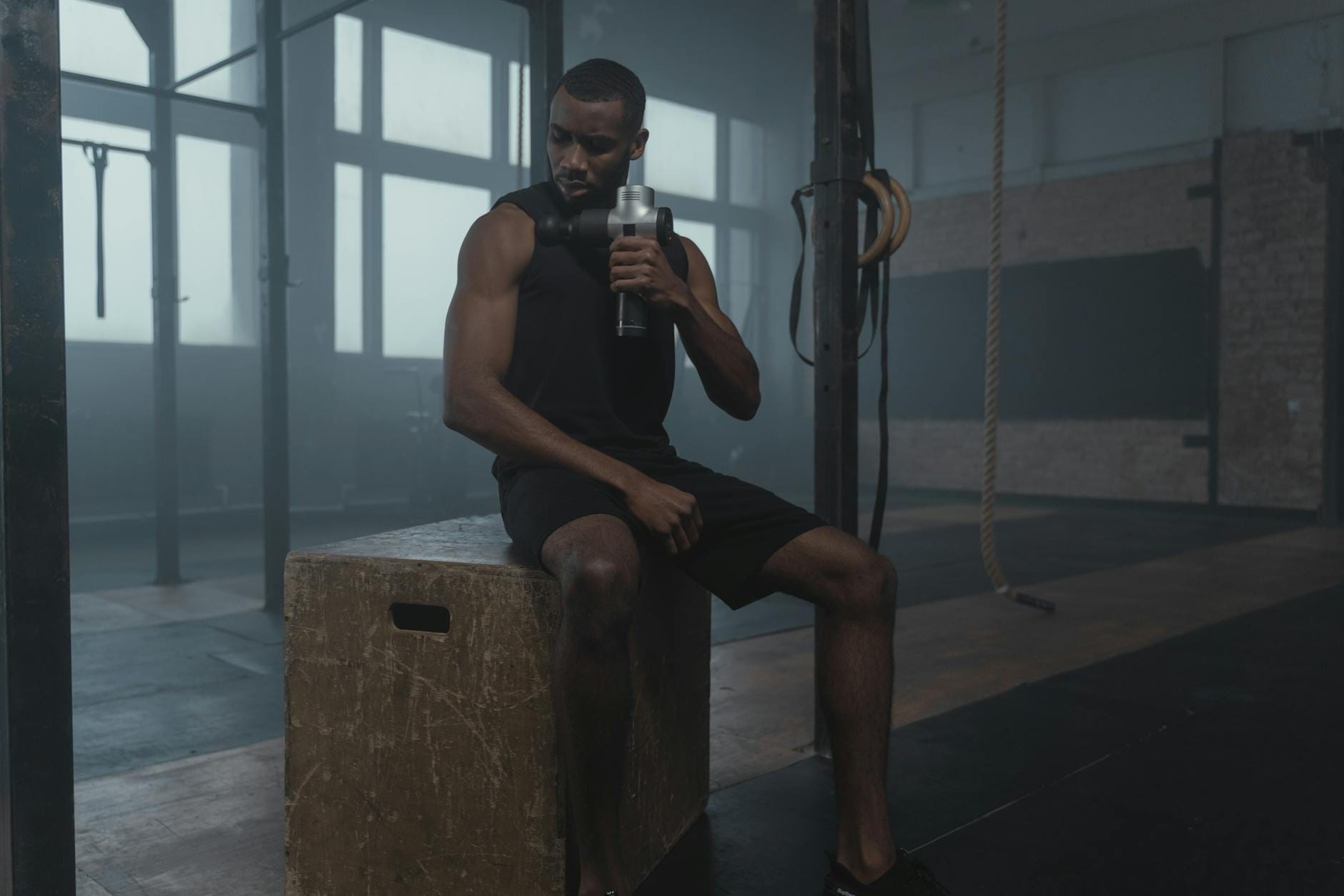 Mężczyzna w siłowni masuje udo pistoletem do masażu podczas regeneracji