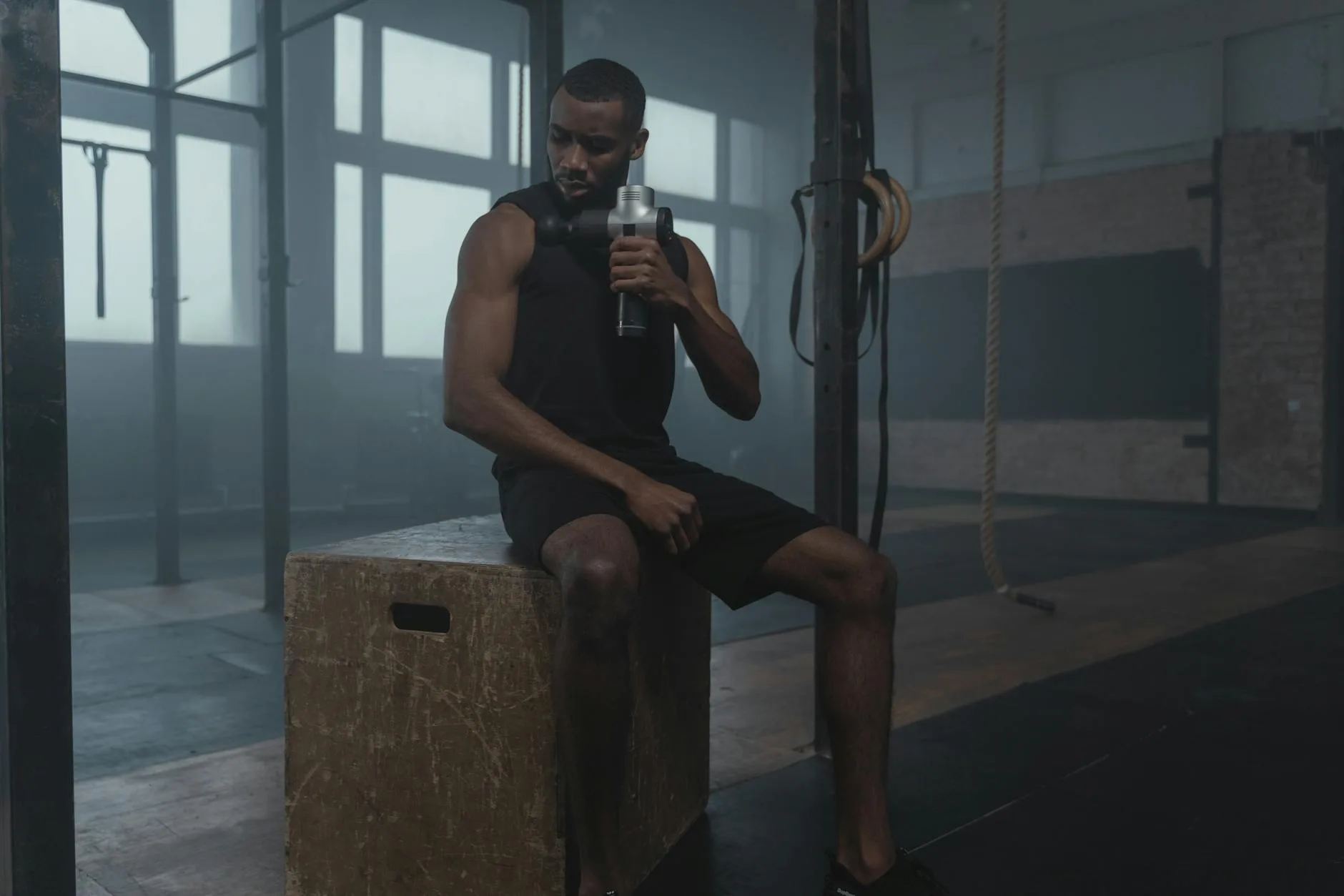 Mężczyzna w siłowni masuje udo pistoletem do masażu podczas regeneracji