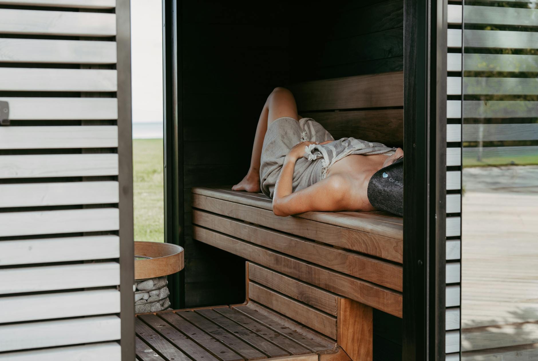 Osoba leżąca w nowoczesnej saunie z ręcznikiem i czapką na głowie