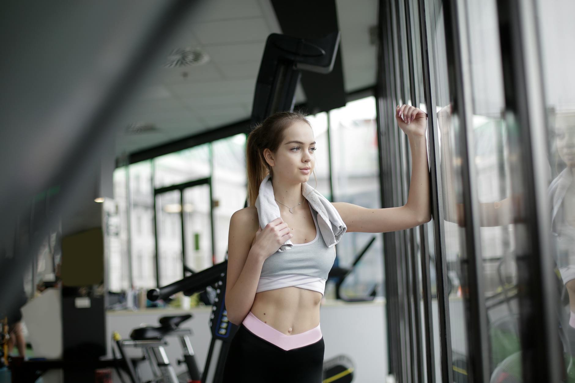Kobieta po treningu patrzy w okno siłowni, myśląc o swoich nawykach