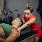 Jak poprawić rotację zewnętrzną barku pod wyciskanie hantli nad głowę Fizjoterapeuta pomaga kobiecie poprawić mobilność barku na siłowni