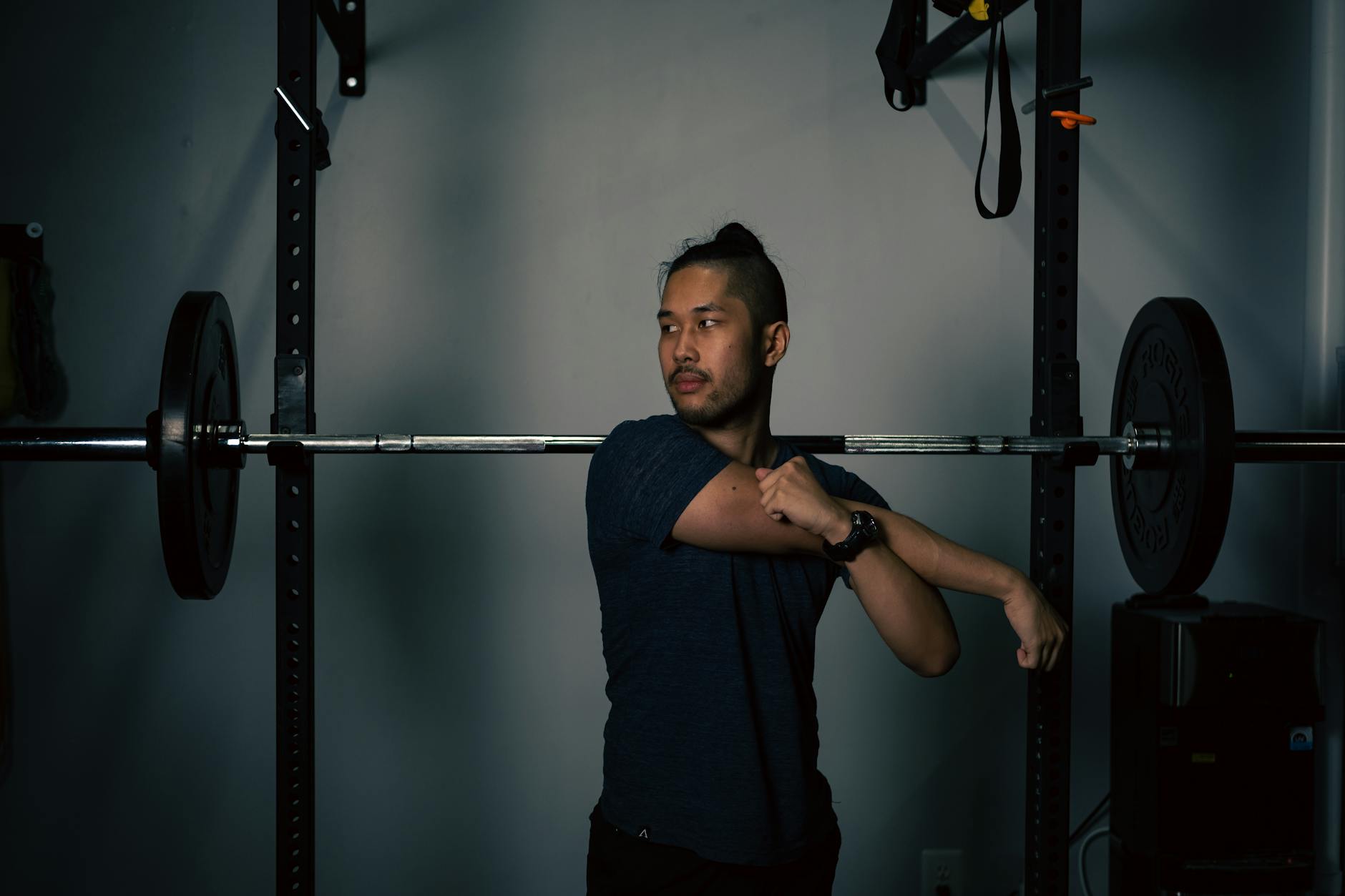 Mężczyzna rozciąga bark przy sztandze w domowej siłowni
