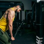 Mężczyzna w żółtym bezrękawniku ćwiczy triceps na wyciągu w siłowni
