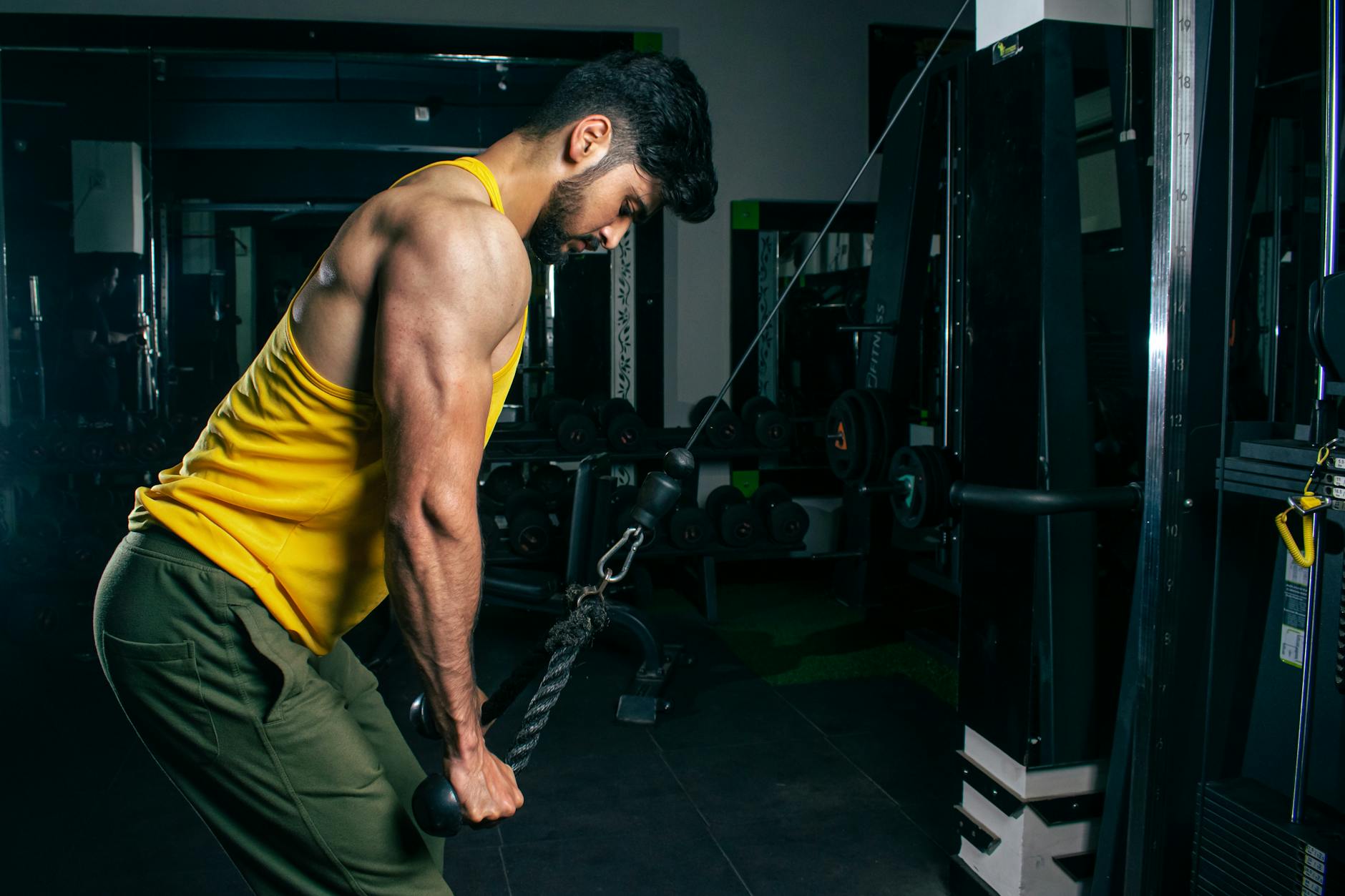 Mężczyzna w żółtym bezrękawniku ćwiczy triceps na wyciągu w siłowni
