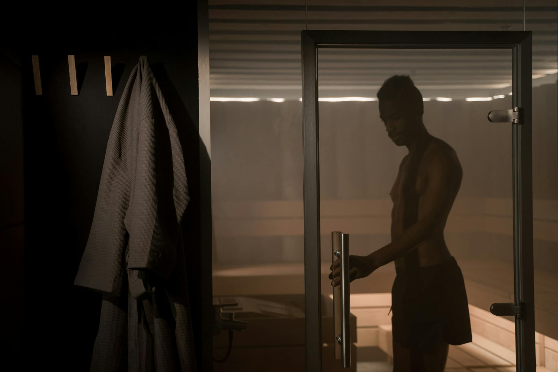 Sauna i mobilność: jak ciepło ułatwia rozciąganie i pracę nad zakresem ruchu Sylwetka mężczyzny wchodzącego do sauny przez szklane drzwi
