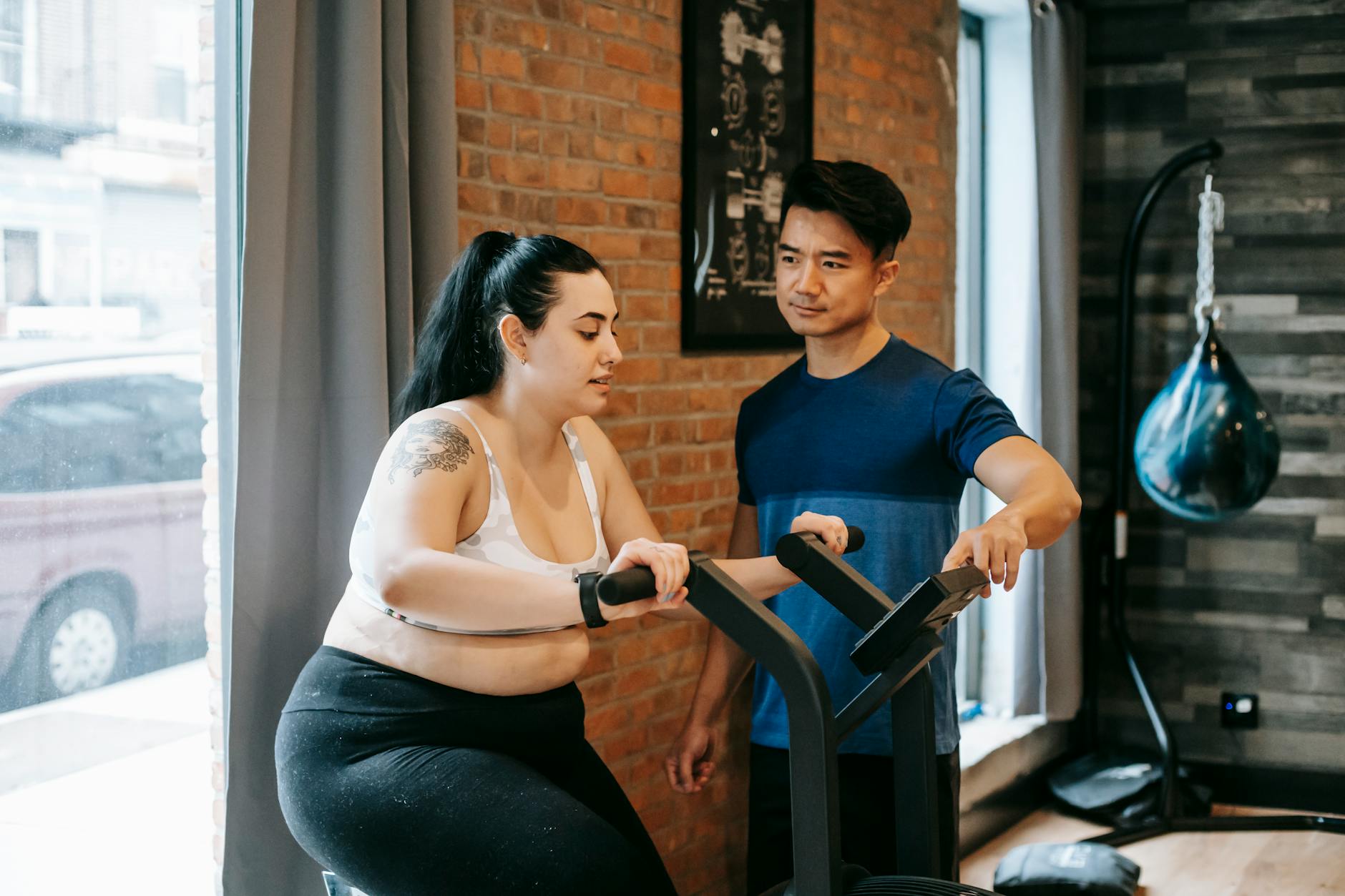 Trener pomaga kobiecie plus size ćwiczyć na rowerku stacjonarnym