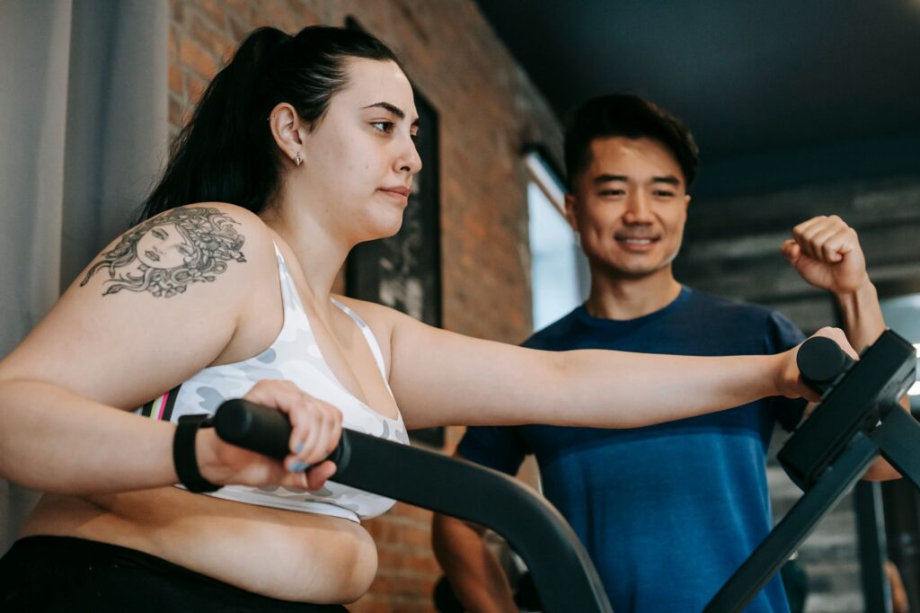 Trener motywuje kobietę ćwiczącą na orbitreku w klubie fitness